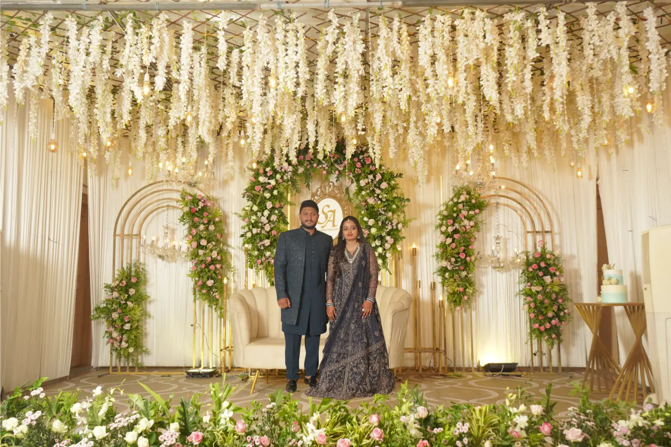 Outdoor wedding aisle lined with white flower arrangements on pedestals under crystal chandeliers